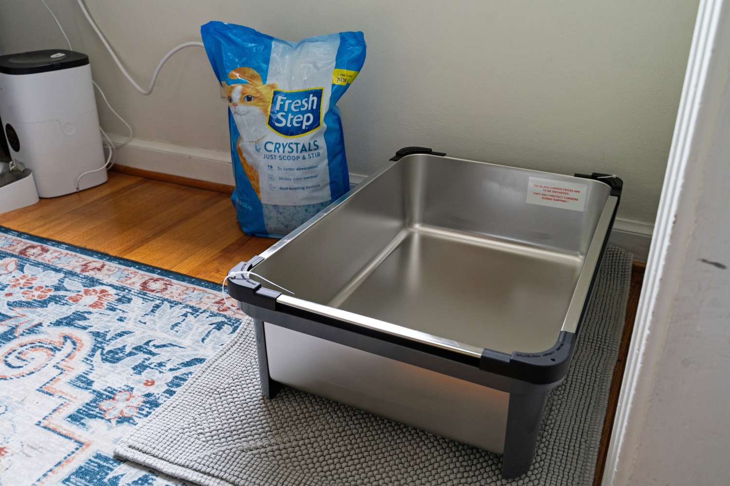 An empty iPrimio Enclosed Sides Stainless Steel Cat XL Litter Box next to a bag of litter