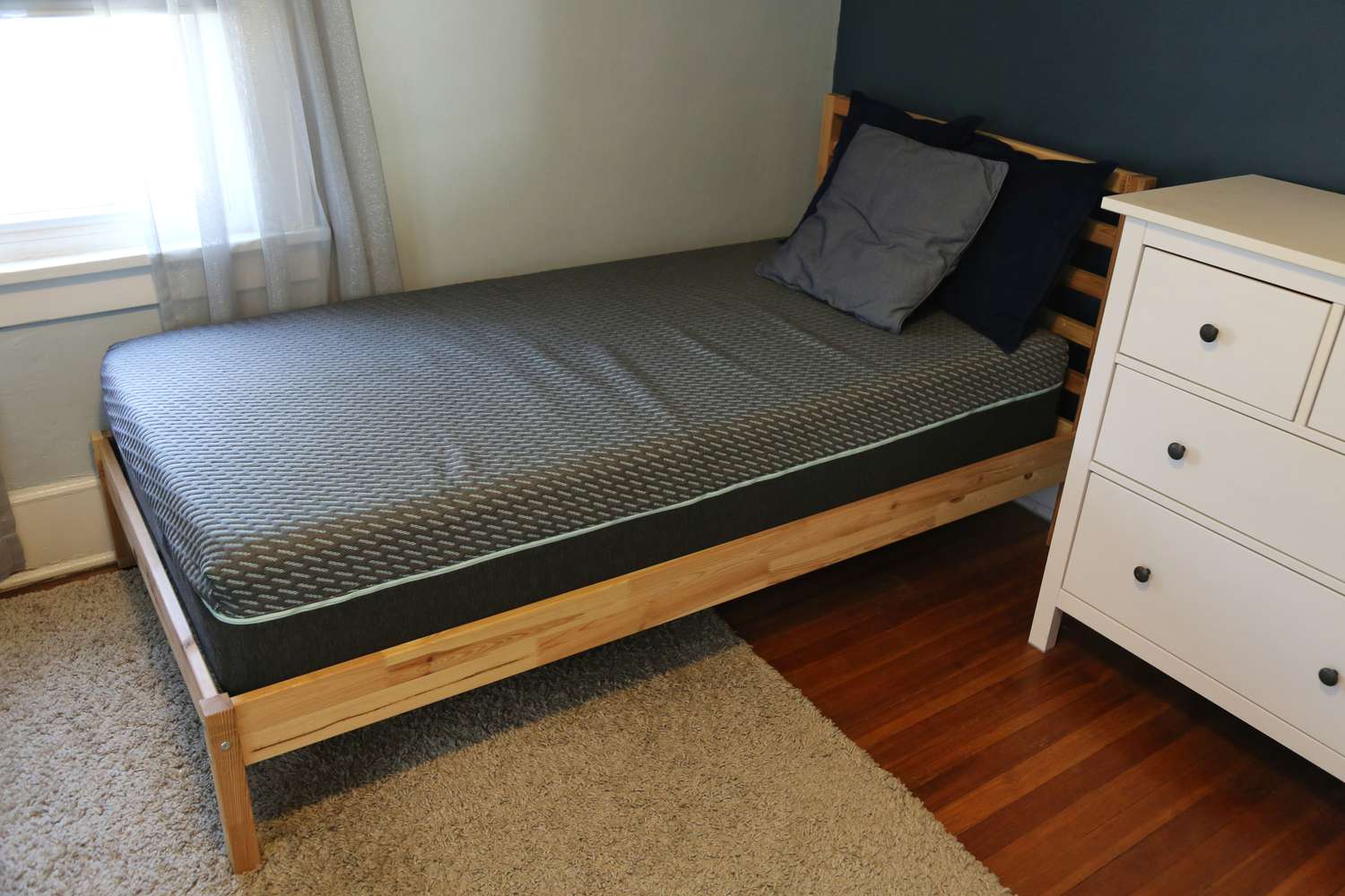 The Tuft & Needle Mint Hybrid Mattress displayed on a wooden bed frame with three pillows