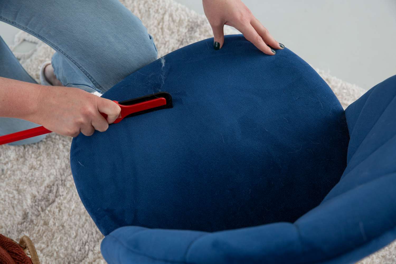 Hands cleaning a plush chair with the Lilly Brush Pro Pet Hair Tool