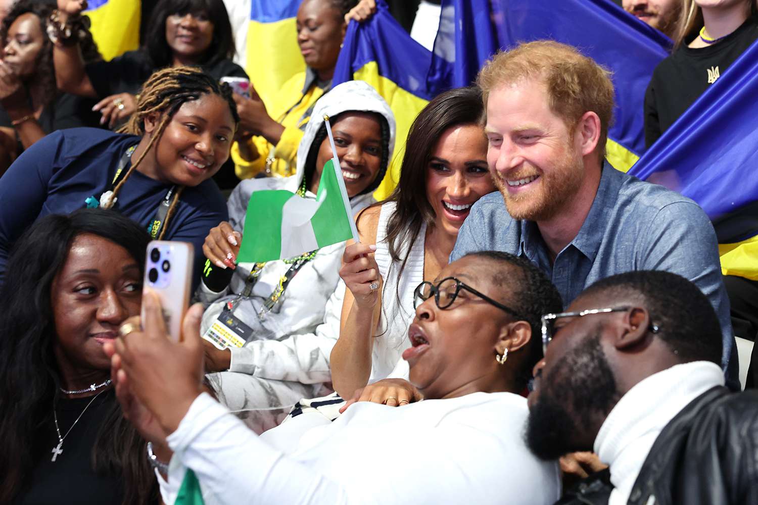 Meghan, Duchess of Sussex Prince, and Prince Harry, Duke of Sussex, take selfies with fans as they attend the Ukraine Nigeria Mixed Team Preliminary Round - Pool A Sitting Volleyball match during day five of the Invictus Games