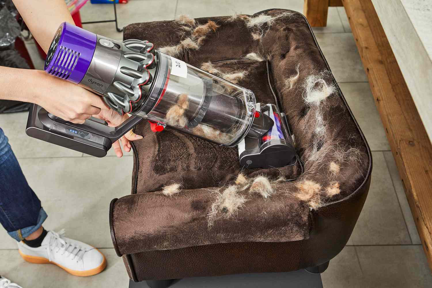 Person using Dyson Cyclone V10 Animal Cordless Stick Vacuum smaller nozzle to clean fur from brown pet couch