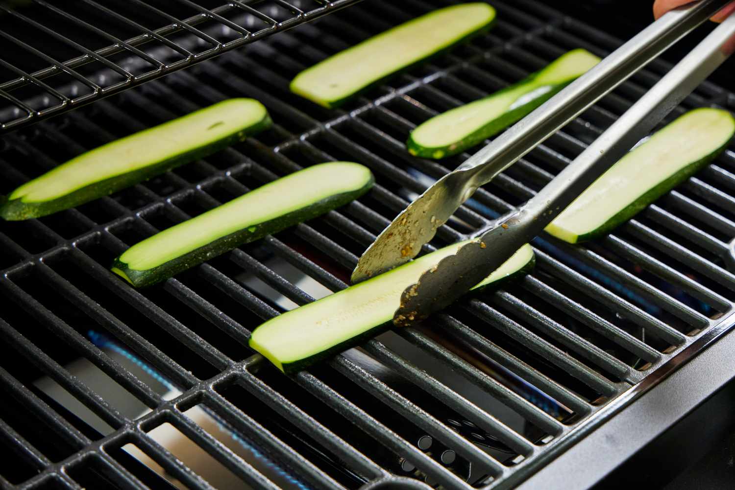 A person grills zucchini on the Nexgrill 4 Burner Propane Gas Grill