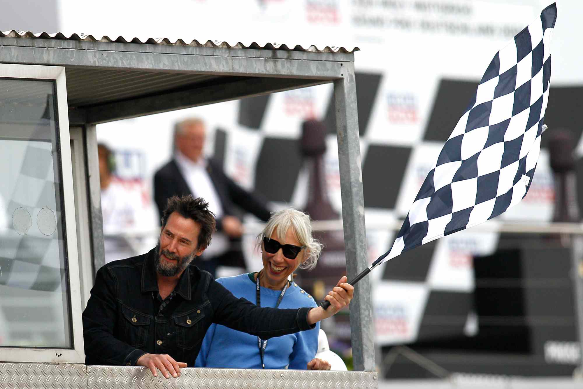  Actor Keanu Reeves and Alexandra Grant wave the checkered flag at the MotoGP of Germany at the Sachsenring Circuit on July 07, 2024