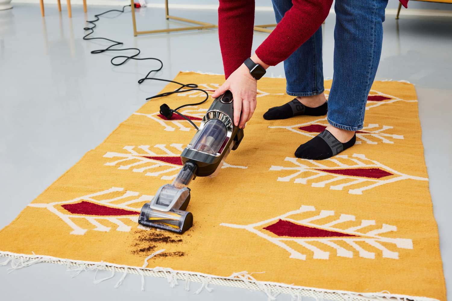 A person vacuums dirt from the 54 Kibo Cypress Mustard Floral Area Rug