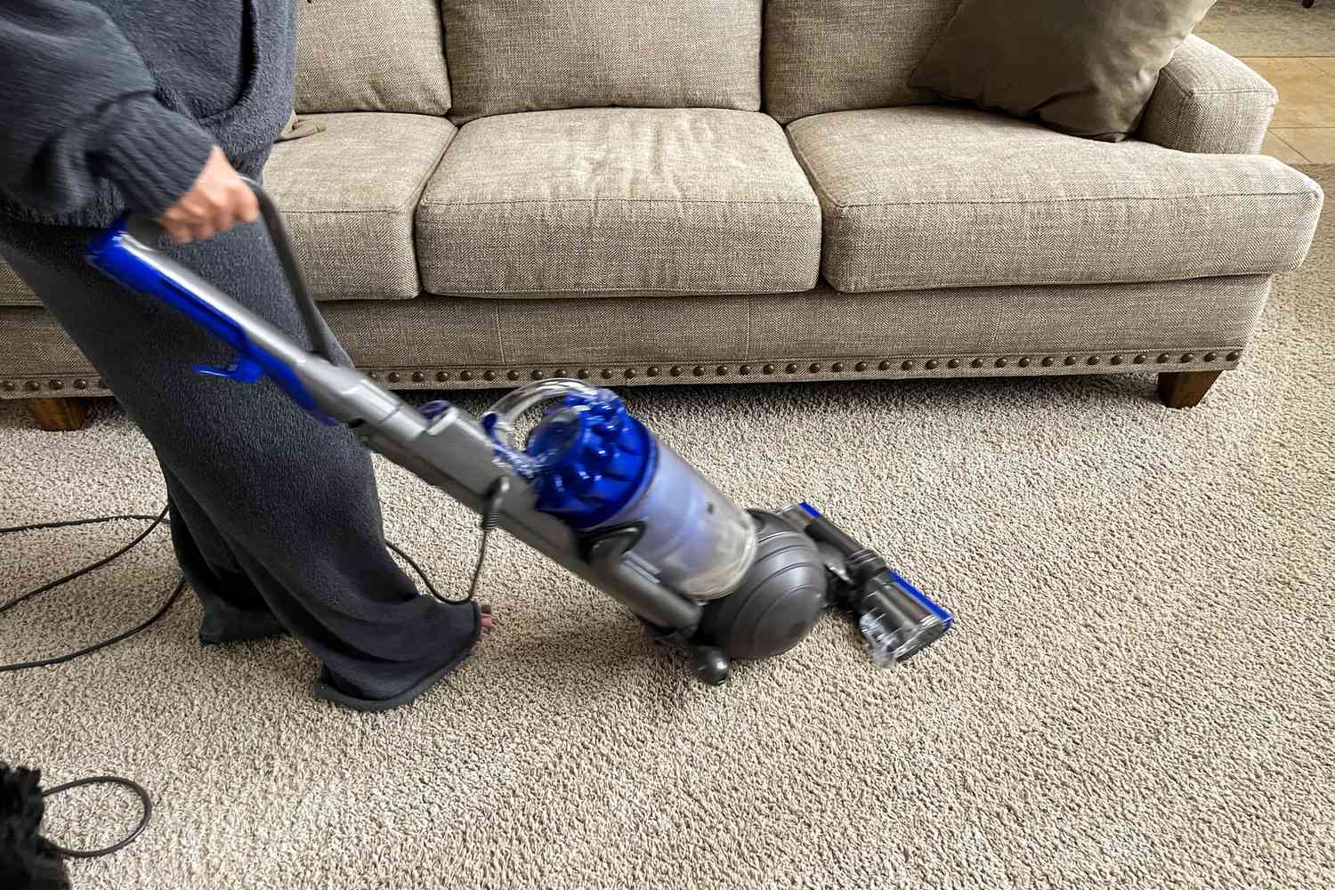 A person uses the Dyson Ball Animal Total Clean to vacuum a carpeted floor