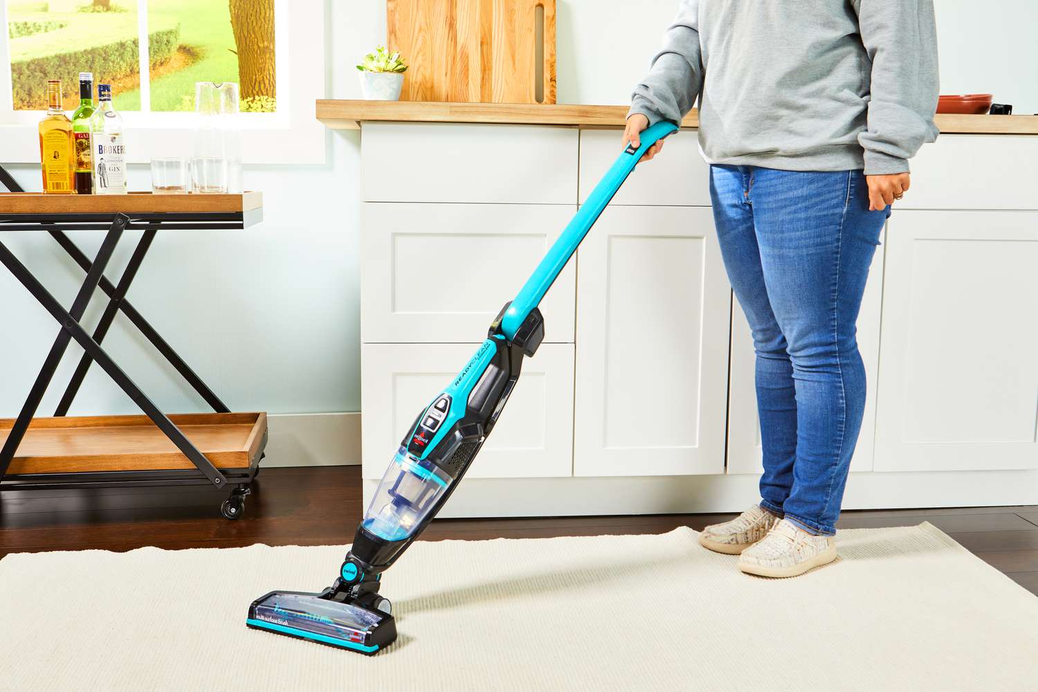A person holding the BISSELL 3061 Featherweight Cordless Stick Vacuum in a kitchen.