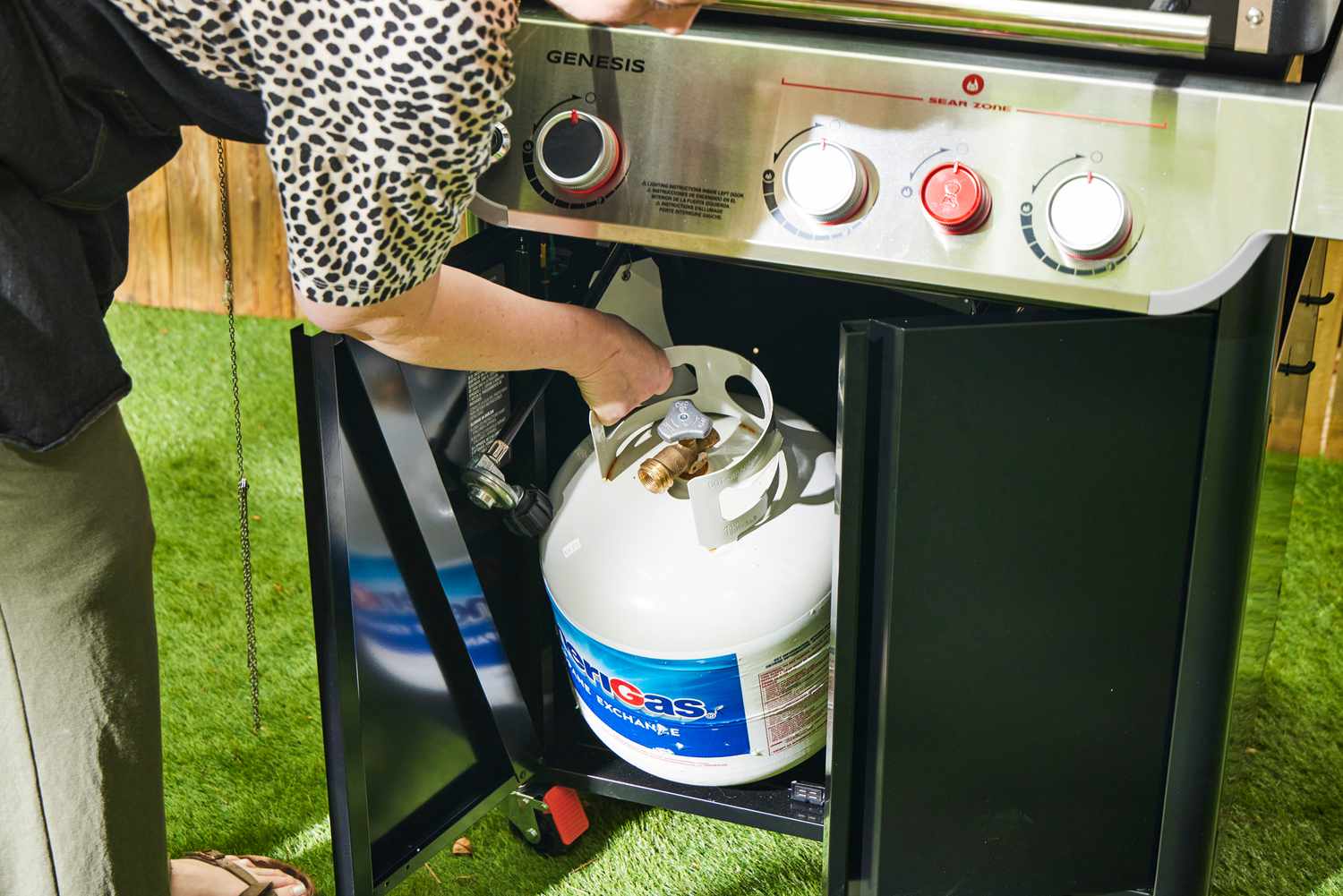 A person places a propane tank inside the Weber Genesis E-325 Liquid Propane Gas Grill