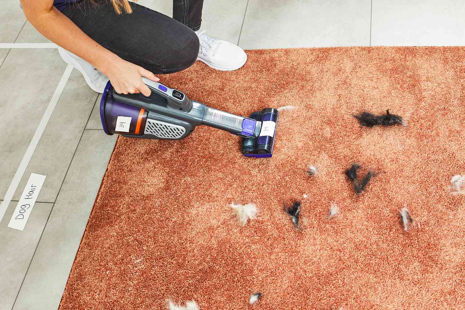 Hand using the Black+Decker Dustbuster AdvancedClean+ Pet Cordless Hand Vacuum Cleaner to clean pet hair from an orange carpet