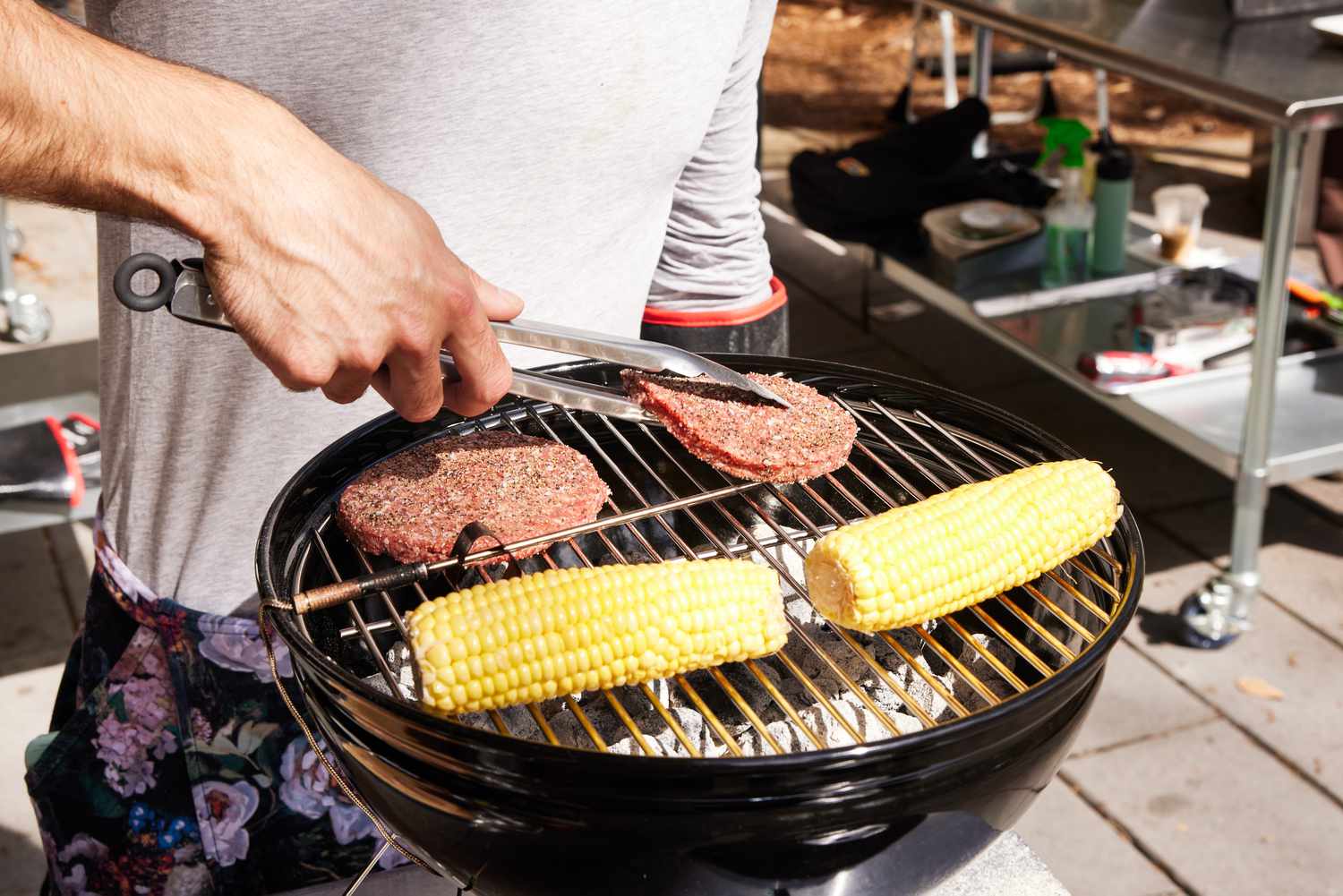 person flipping burgers on Weber Smokey Joe Charcoal Grill next to corn