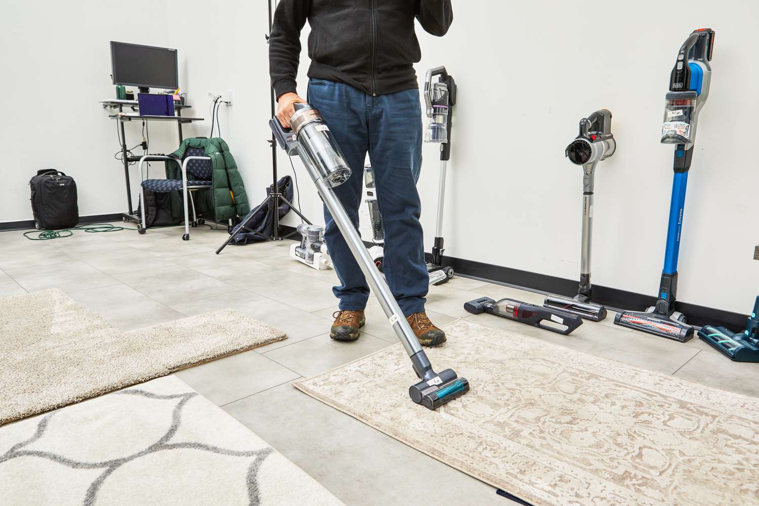 Person cleaning a rug with a Samsung Jet 75 Cordless Stick Vacuum with other vacuums in background