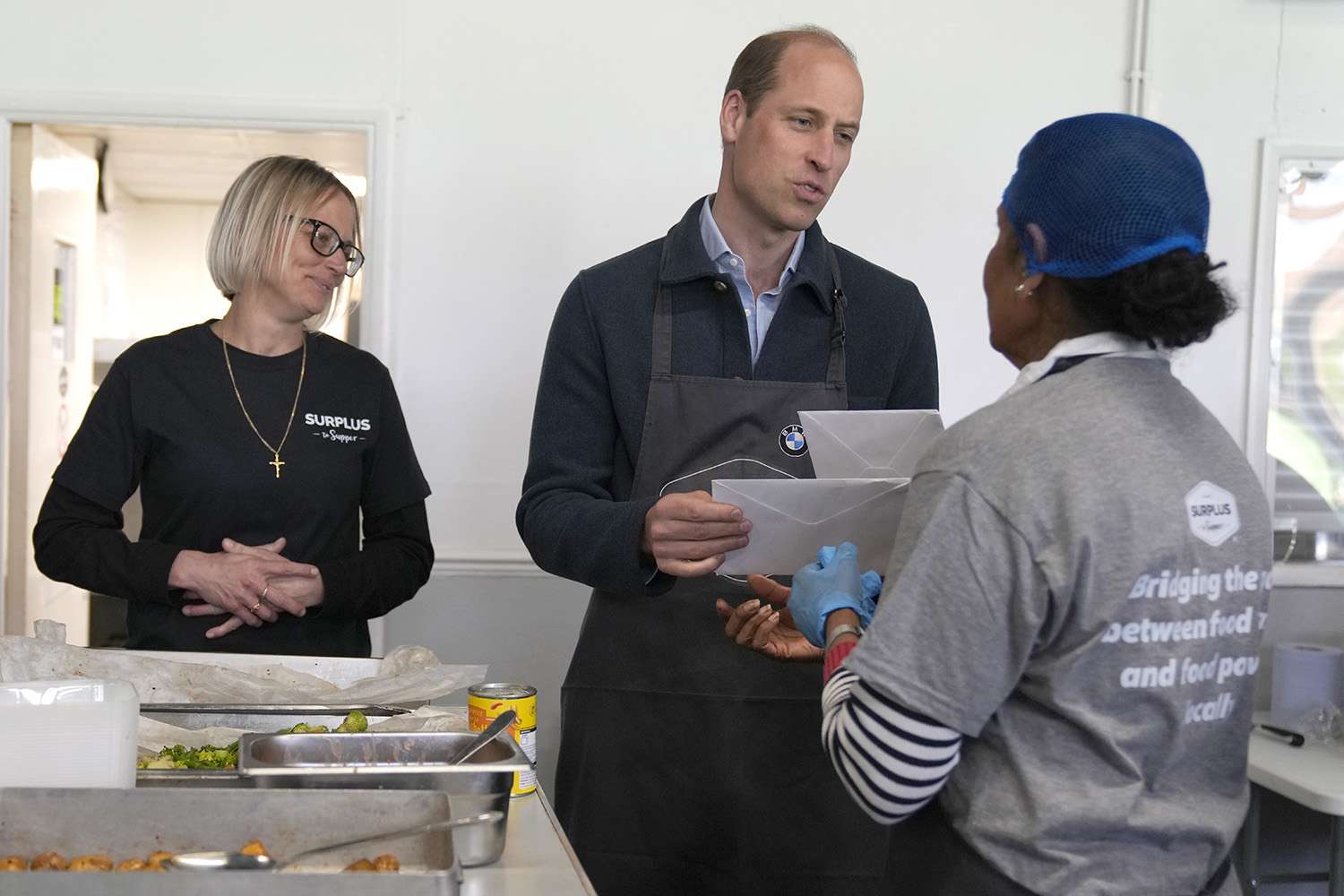 Prince William, Prince of Wales is given cards for his wife Catherine, Princess of Wales by volunteer Rachel Candappa as Claire Hopkins, Operations Director looks on (L) during a visit to Surplus to Supper, in Sunbury-on-Thames on April 18, 2024