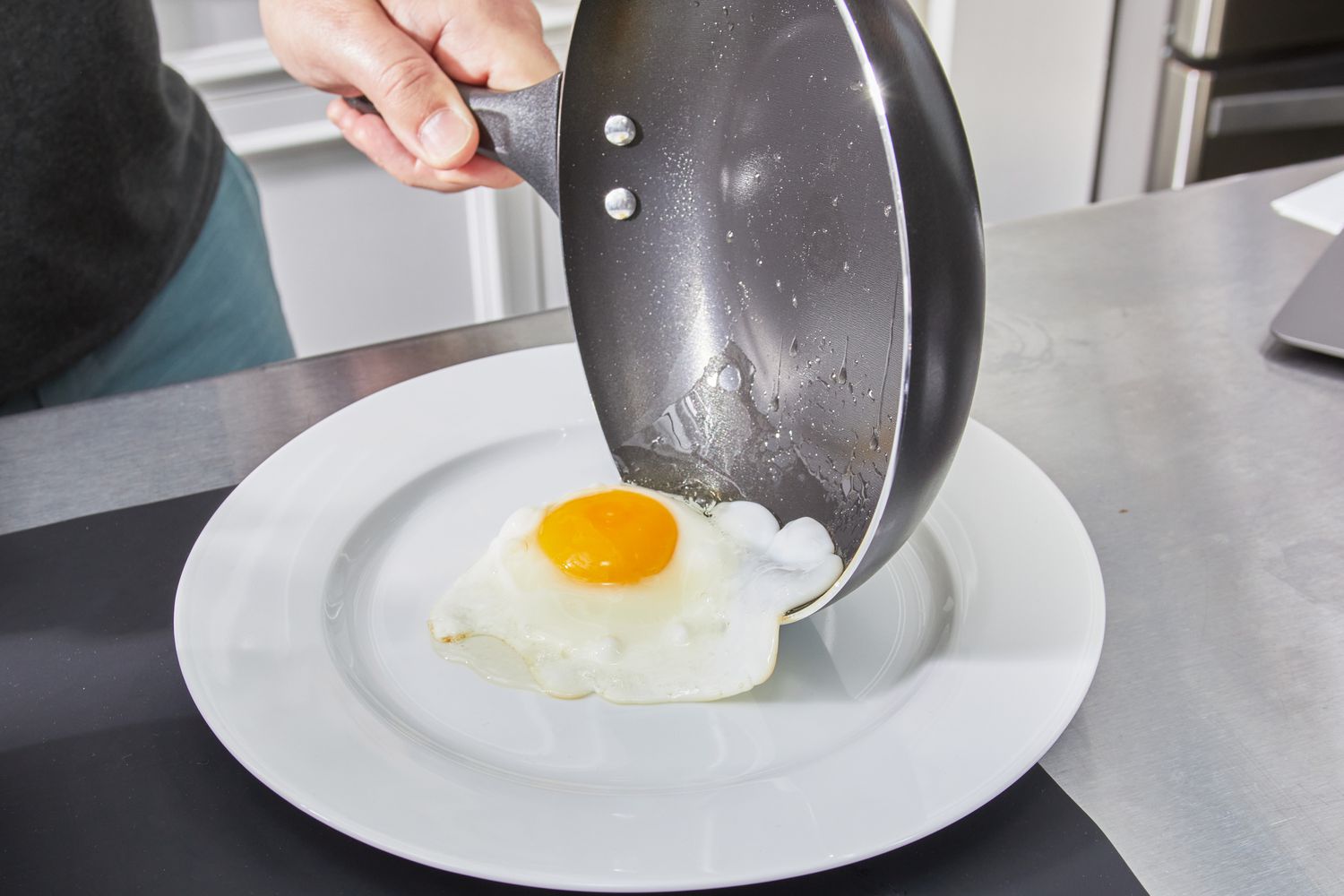 Hand sliding a cooked egg from the Farberware Dishwasher Safe Nonstick 15 Piece Cookware Pots and Pans Set on to a plate