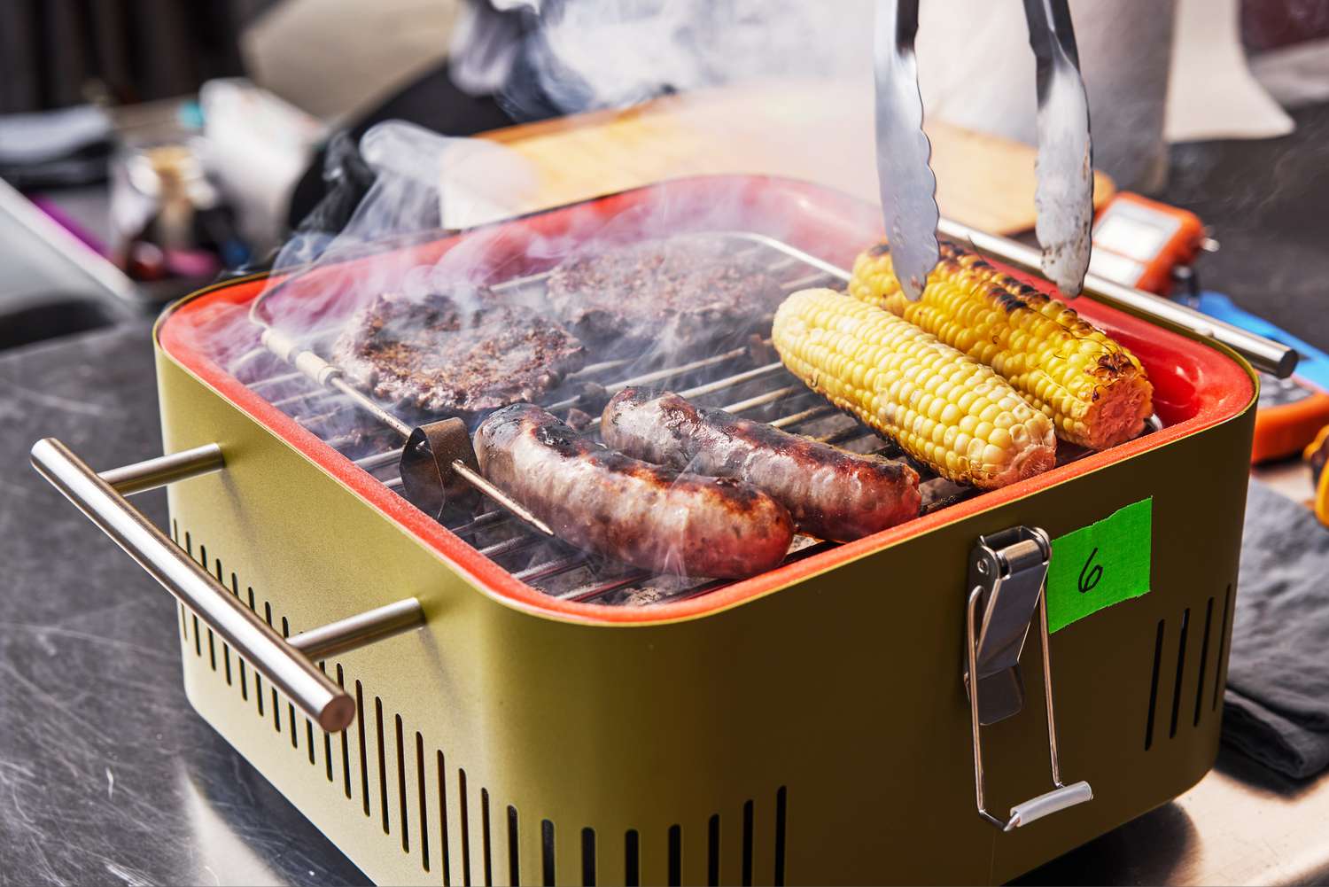Closeup of sausages, burger and corn cooking on the Everdure CUBE Portable Charcoal Grill 