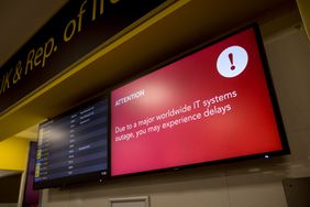 A screen displays an announcement on possible travel delays due to a global IT outage Gatwick Airport