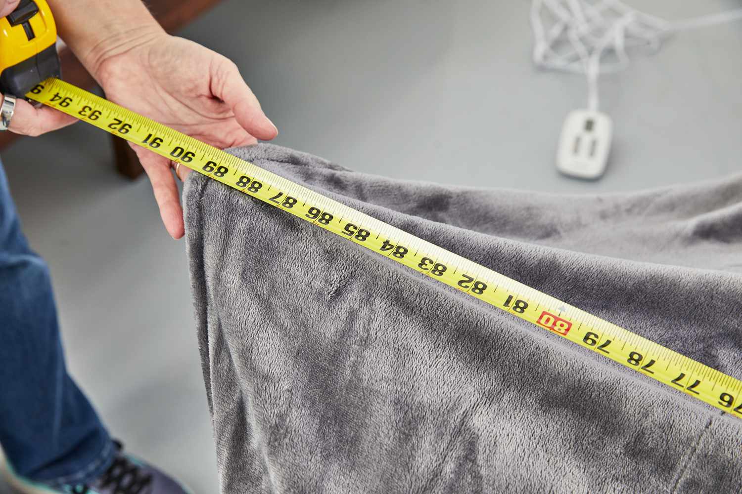 Close-up of person measuring Brookstone N-A-P Heated Plush Blanket with measuring tape