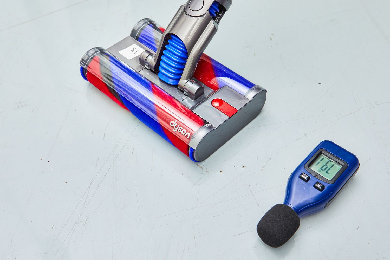 Dyson Omni-Glide Cordless Vacuum next to a decibel meter on grey flooring