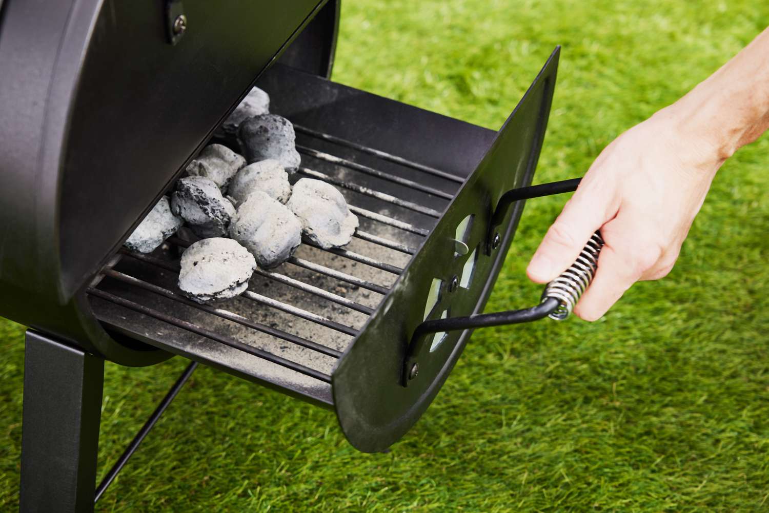 hand pulls out charcoal tray of Dyna-Glo Signature Series Portable Tabletop Charcoal Grill 