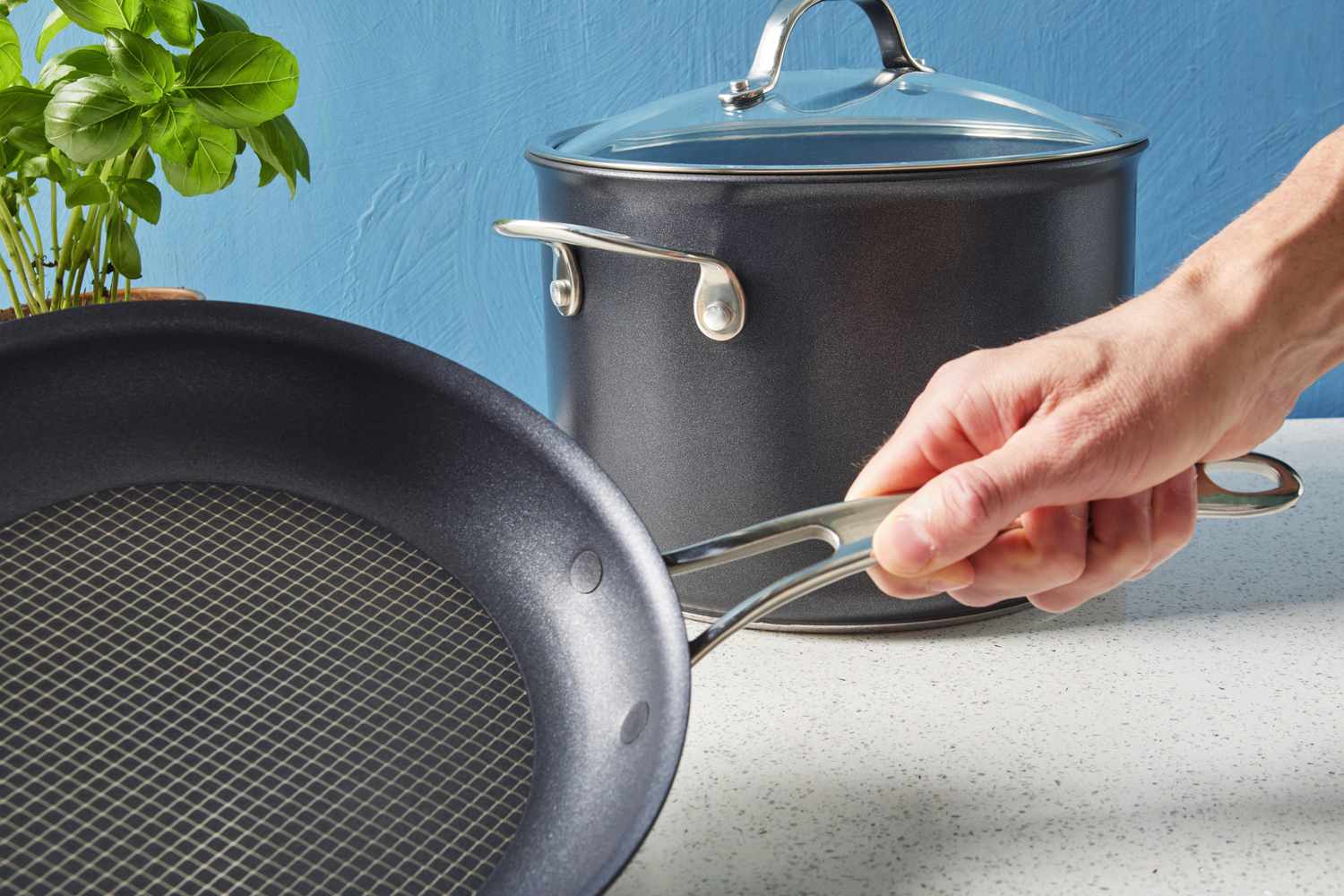 Hand holding handle of Anolon X Hybrid 10-Piece Nonstick Cookware Set frying pan while displayed on countertop