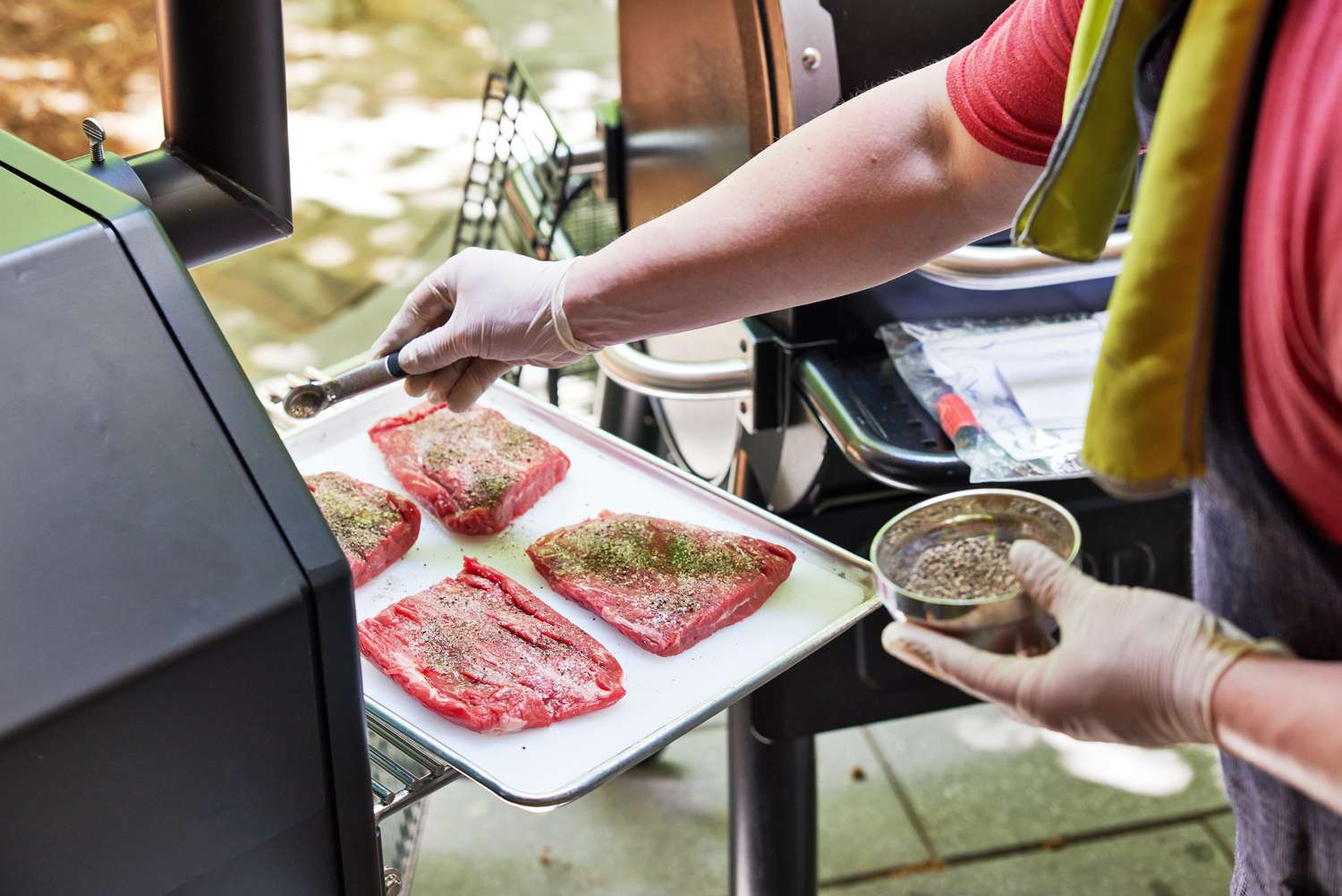 Person seasoning a tray of meat sitting on the side rack of a Yoder Smokers YS640S Pellet Grill