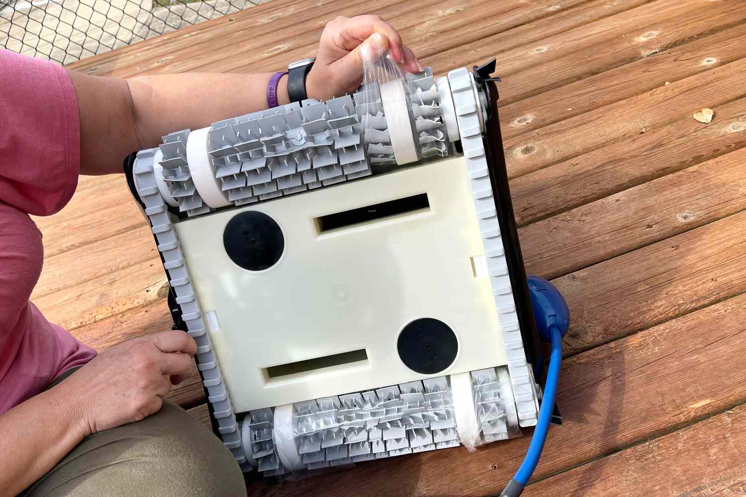 Person showing bottom of Dolphin Nautilus CC Plus Robotic Pool Cleaner on wooden deck