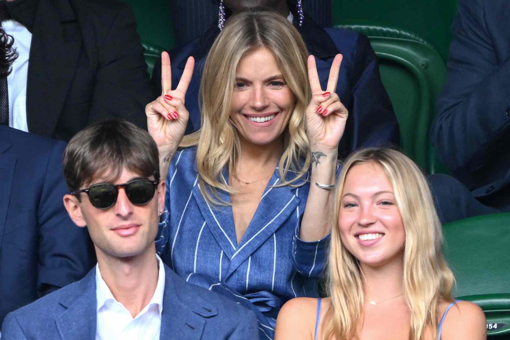 Sienna Miller gestures with the double peace sign and Yoni Helbitz and Lila Moss as they attend day seven of the Wimbledon Tennis Championships at the All England Lawn Tennis and Croquet Club on July 09, 2023