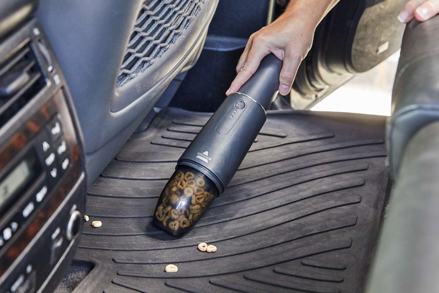 hand using BISSELL AeroSlim Lithium Ion Cordless Handheld Vacuum to clean car floor