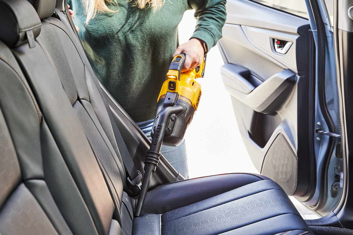 Person vacuuming the back seat of a car with the Dewalt 20-Volt Cordless Handheld Vacuum