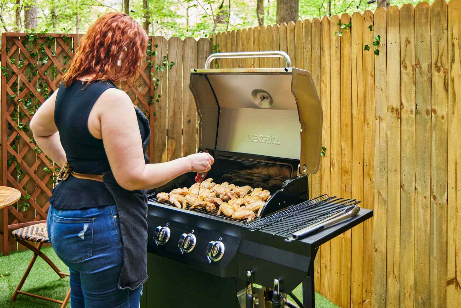 A person checks the temperature chicken cooking in the Nexgrill 4 Burner Propane Gas Grill