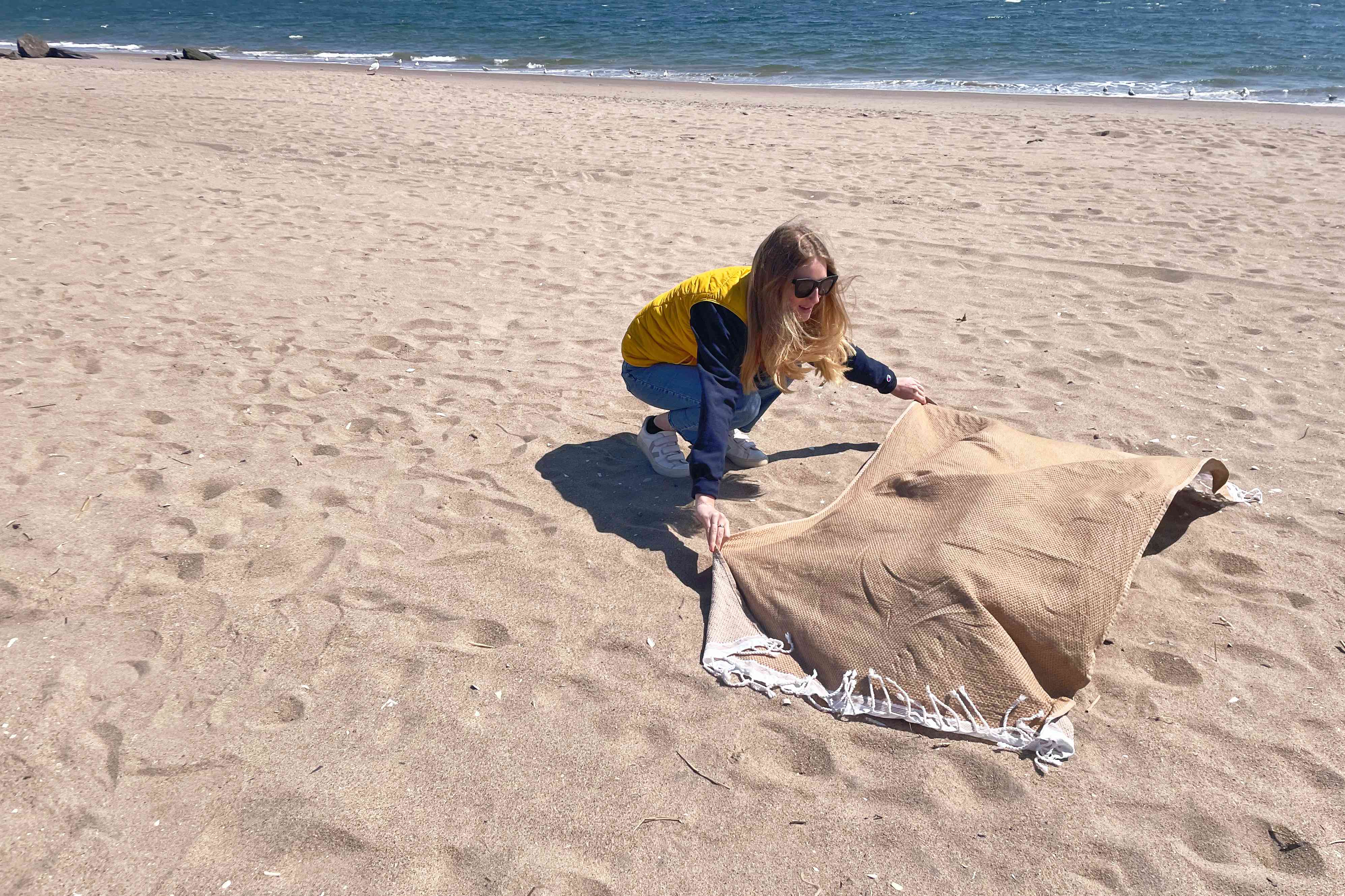 A person puts the Coyuchi Mediterranean Organic Towel on a sandy beach.