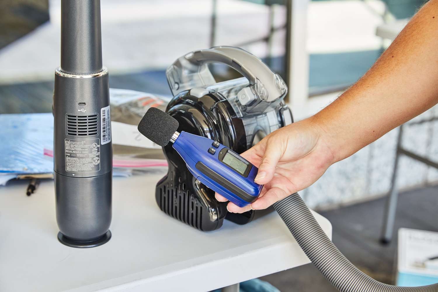 Hand holding a sound level meter next to the Black+Decker Flex Cordless Handheld Vacuum