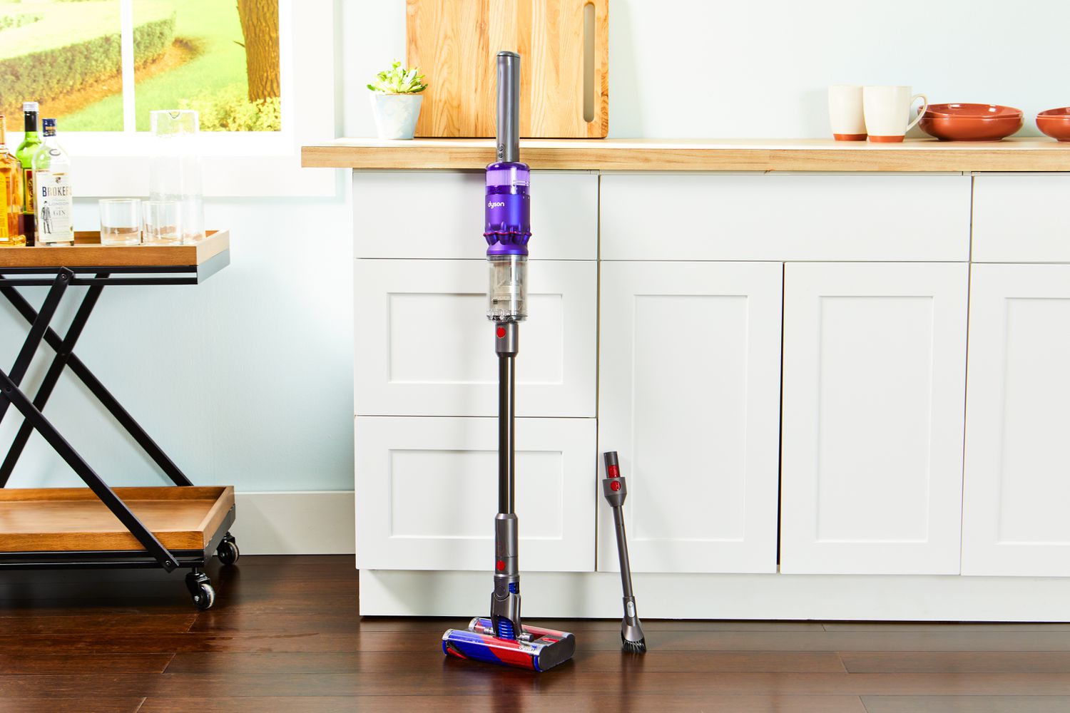 Dyson Omni-Glide+ Cordless Vacuum leaned against the counter with an extra nozzle beside it