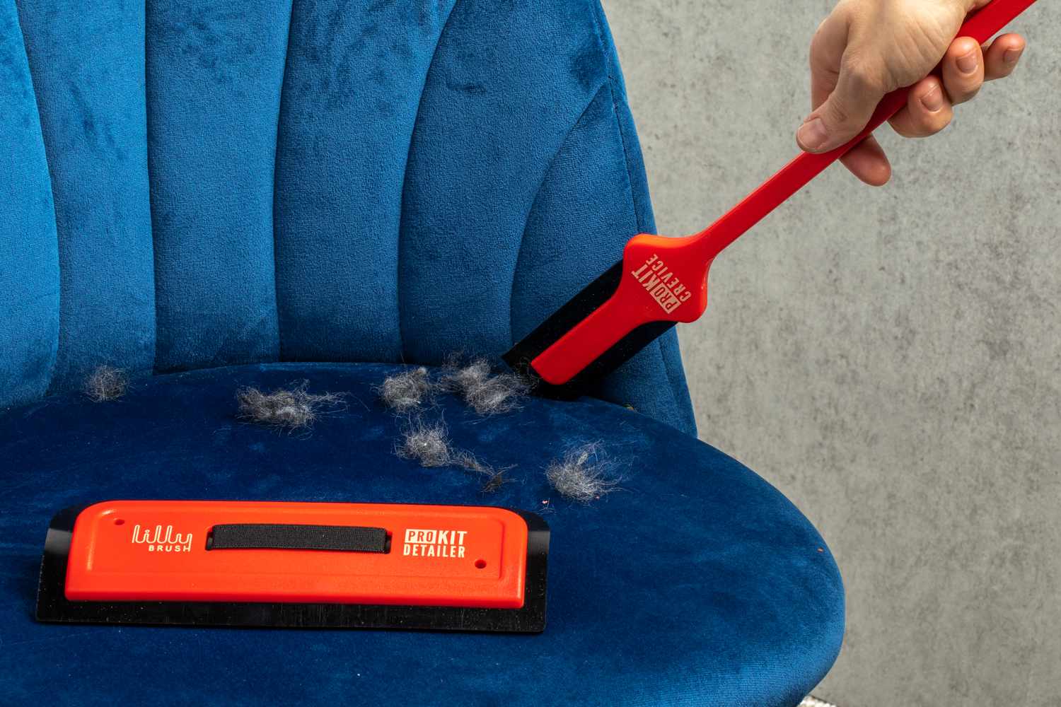 Hand running a Lilly Brush Pro Pet Hair Tool through the crevice of a chair