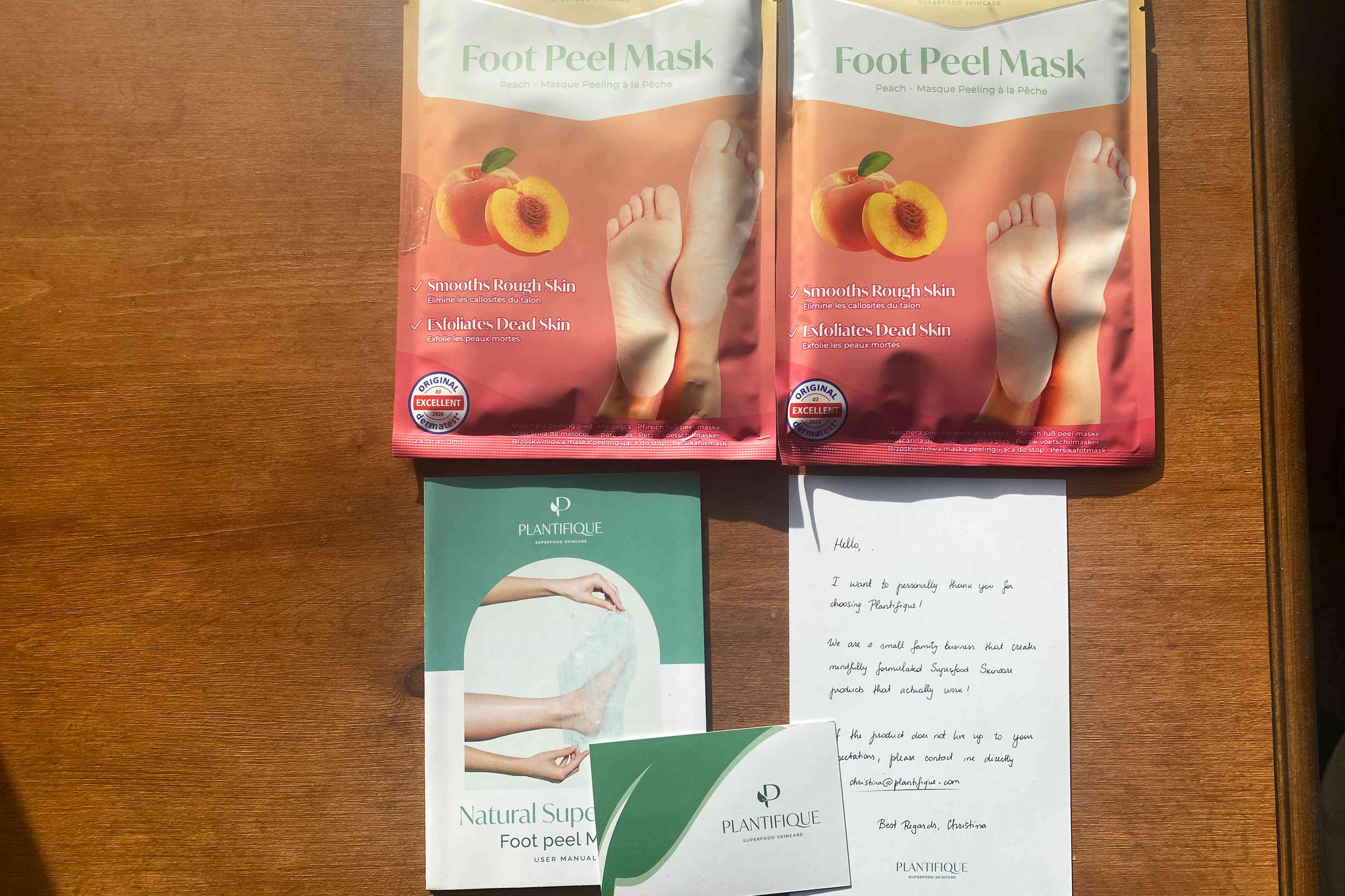 PLANTIFIQUE Peach Foot Peeling Masks in their packaging and sitting on a table next to the instructions