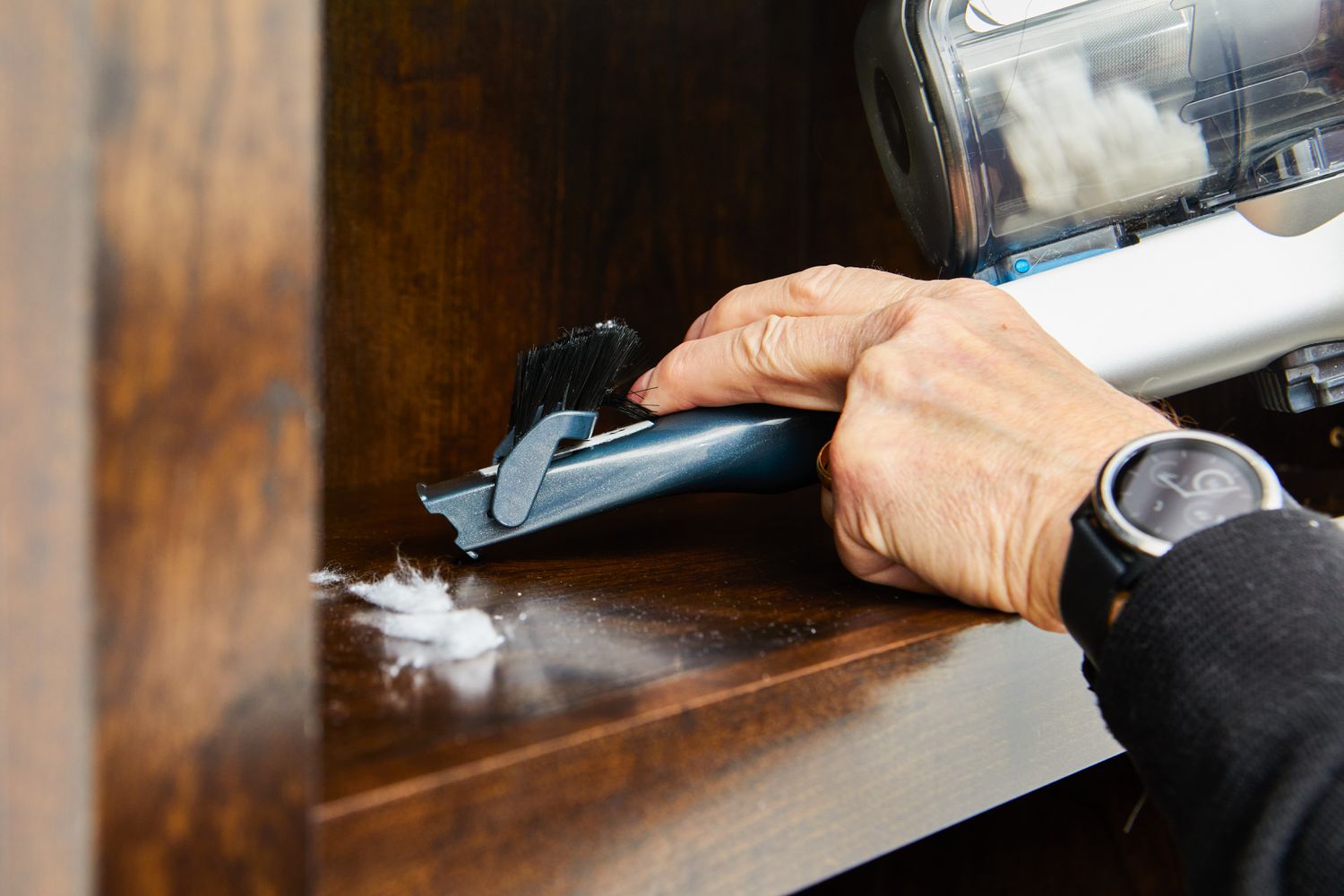 Hand using the BLACK+DECKER Powerseries Extreme Cordless Stick Vacuum Cleaner to clean a shelf