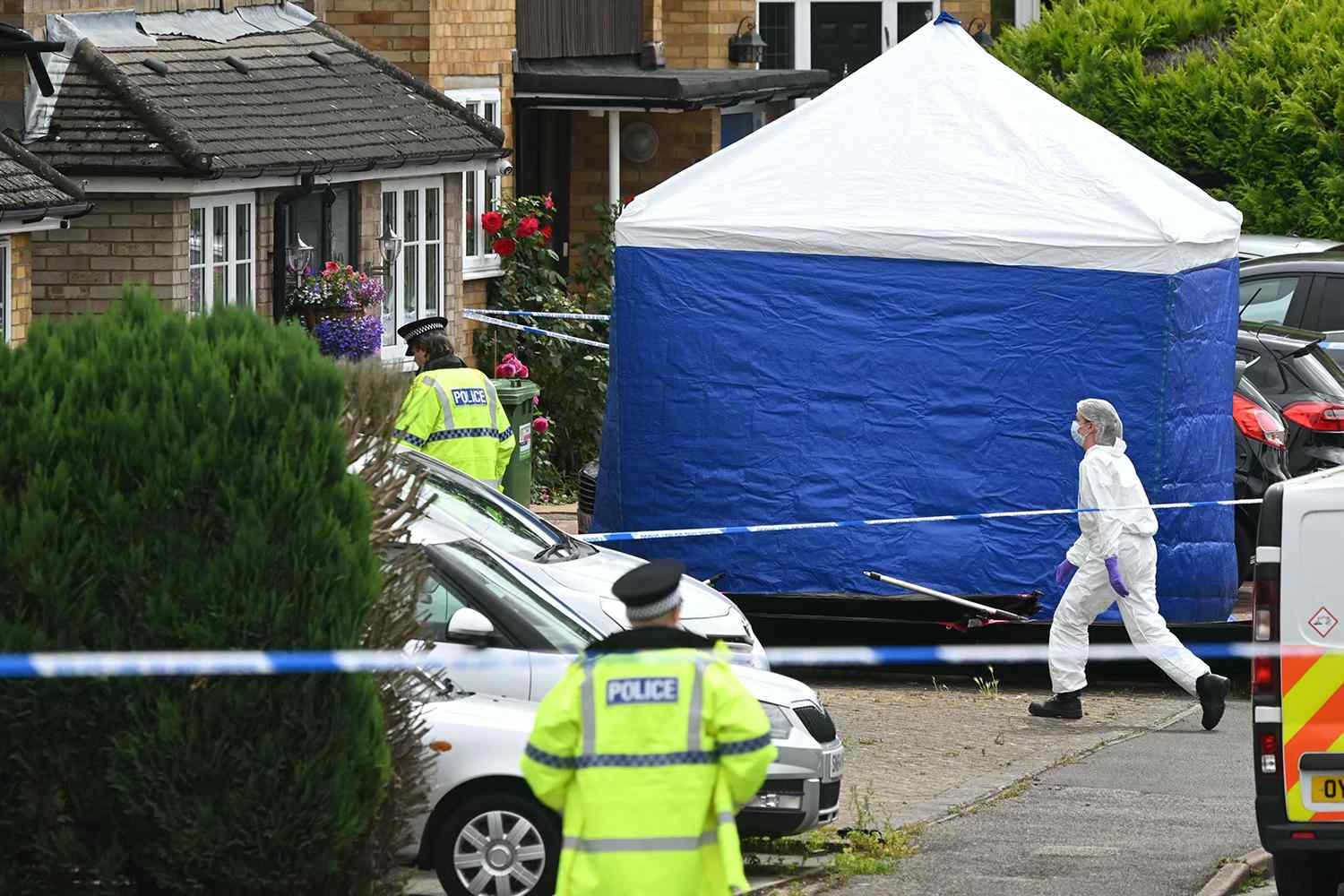 A member of the forensic team walks past a tent set up behind a cordon at Ashley Close in Bushey in the borough of Hertfordshire, north of London, on July 10, 2024 after a triple "crossbow attack" murder.