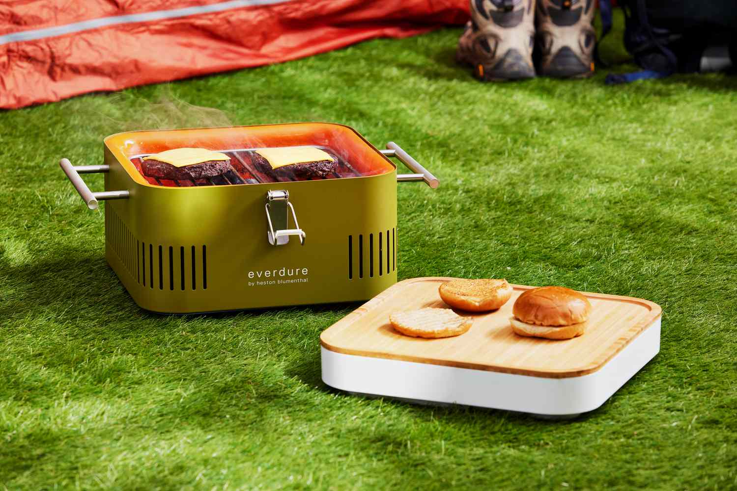 Everdure CUBE Portable Charcoal Grill displayed on gras with lid and burger buns