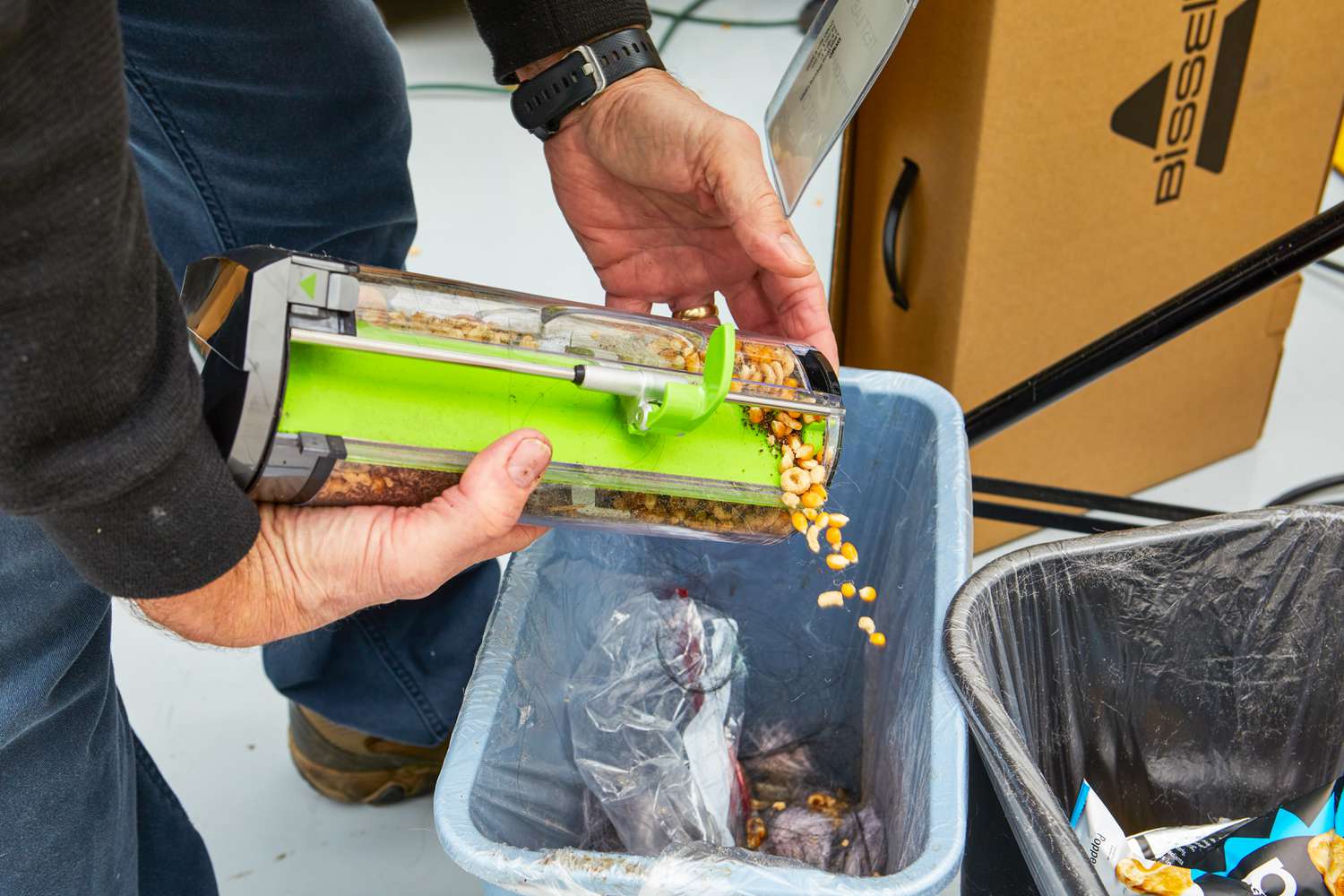 A person empties the filled canister from the Bissell 1984 Air Ram Cordless Vacuum into the trash.