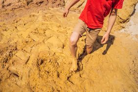 Unlucky person standing in natural quicksand river, clay sediments, sinking, drowning quick sand, stuck in the soil, trapped and stuck concept.
