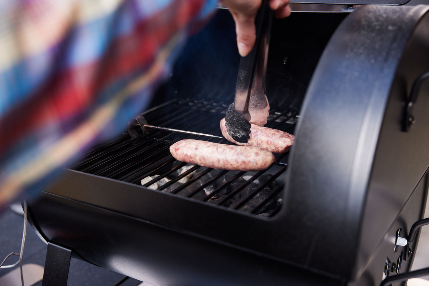 tongs grabbing sausage on Dyna-Glo Portable Tabletop Charcoal Grill