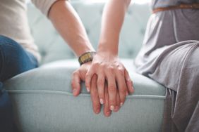 Waist photo of man and woman holding hands while sitting on a couch