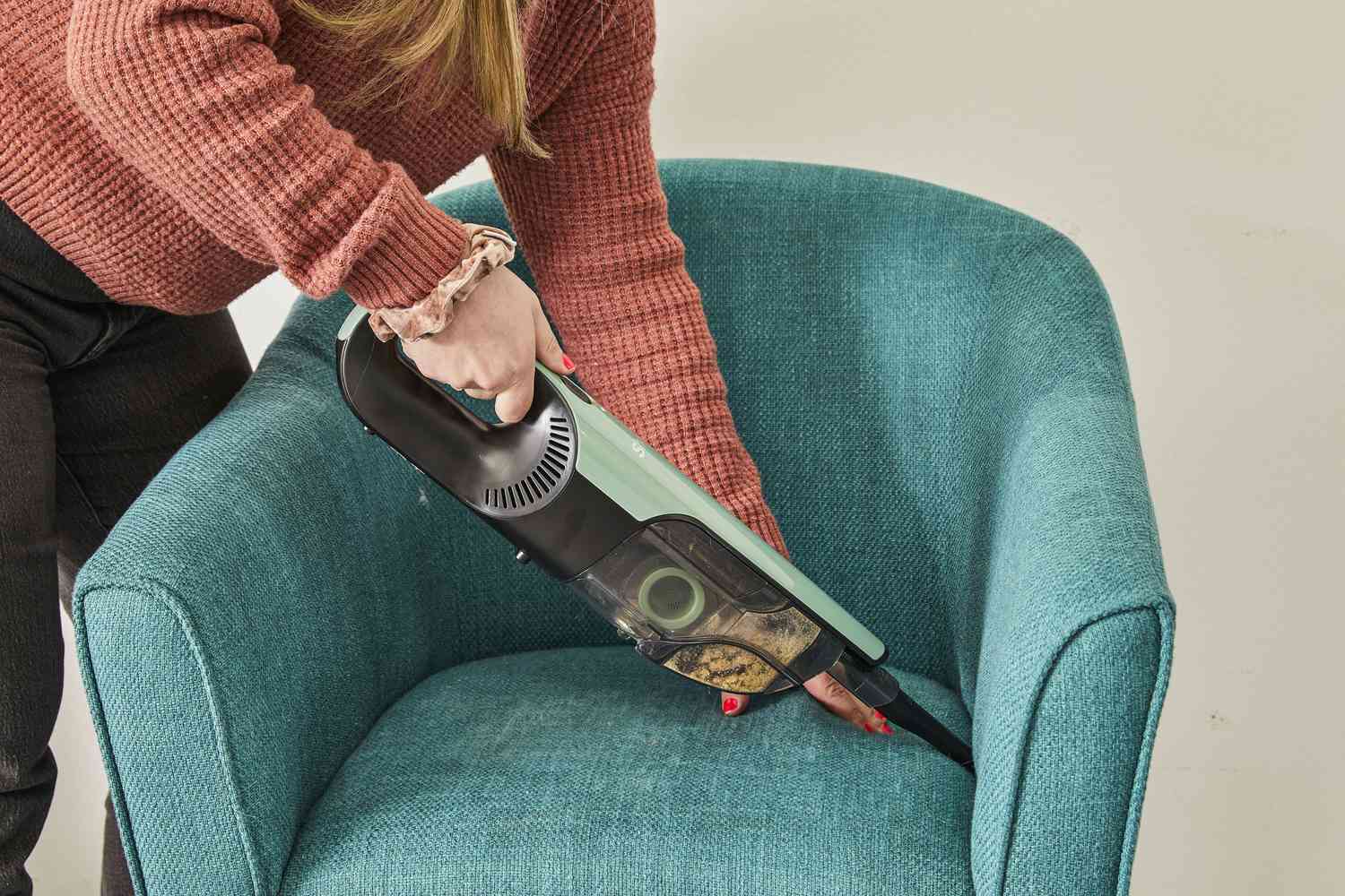 Hands using Shark UltraCyclone Pro Cordless Handheld Vacuum to clean corners of upholstered chair