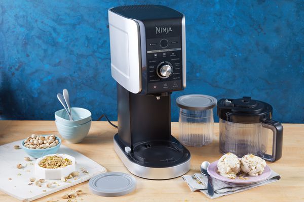 Ninja Creami Deluxe 11-in-1 XL Ice Cream Maker on a counter surrounded by it's accessories and finished ice cream