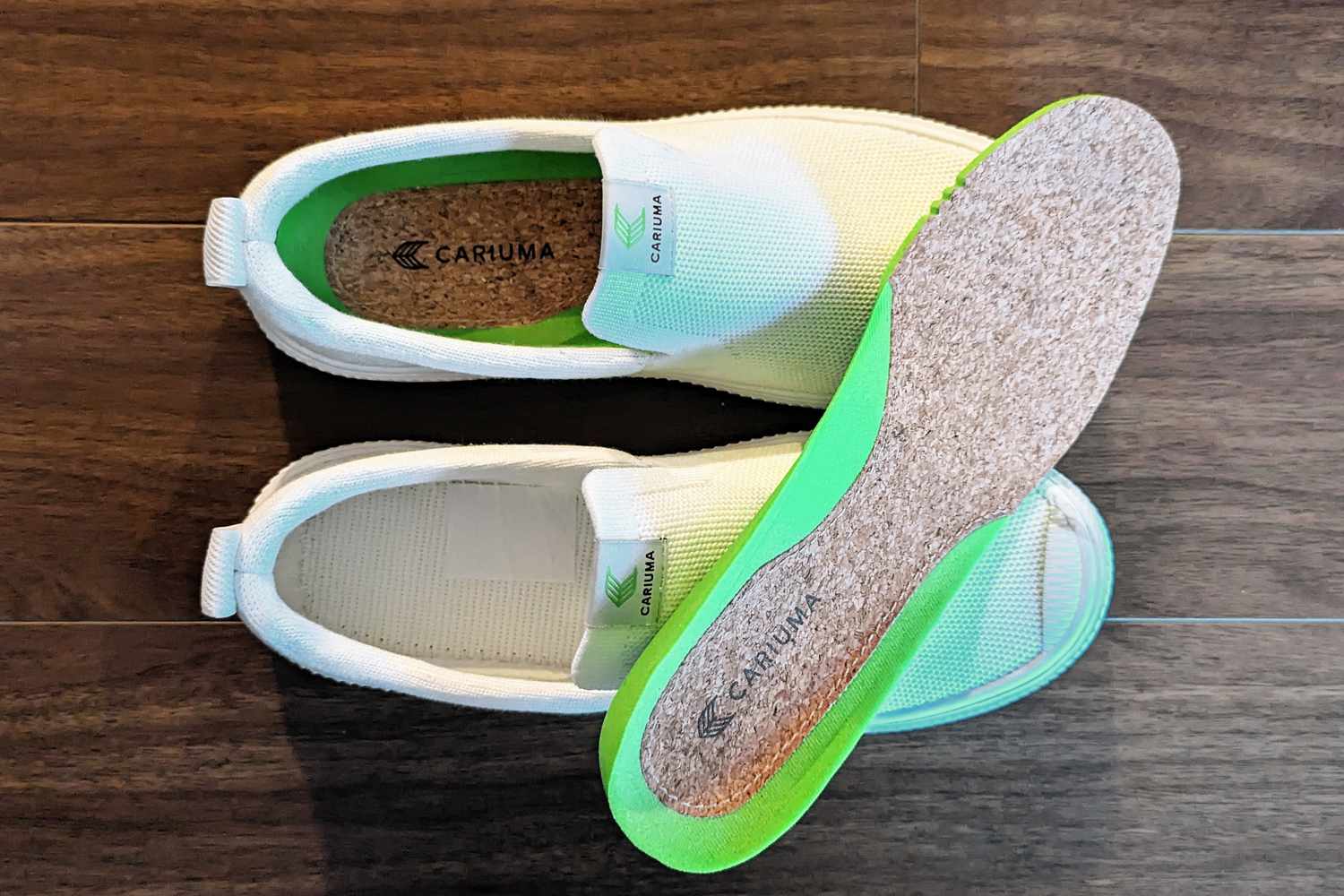 Cariuma IBI Slip Ons sitting on a wood floor with the insole laying on top of the shoes