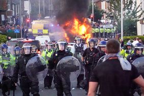 Riot police hold back protesters near a burning police vehicle after disorder broke out on July 30, 2024 in Southport, England.