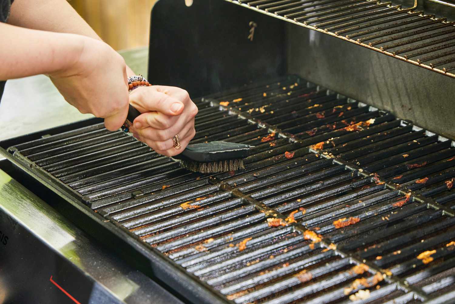 A person cleans the Weber Genesis E-325 Liquid Propane Gas Grill with a grill brush