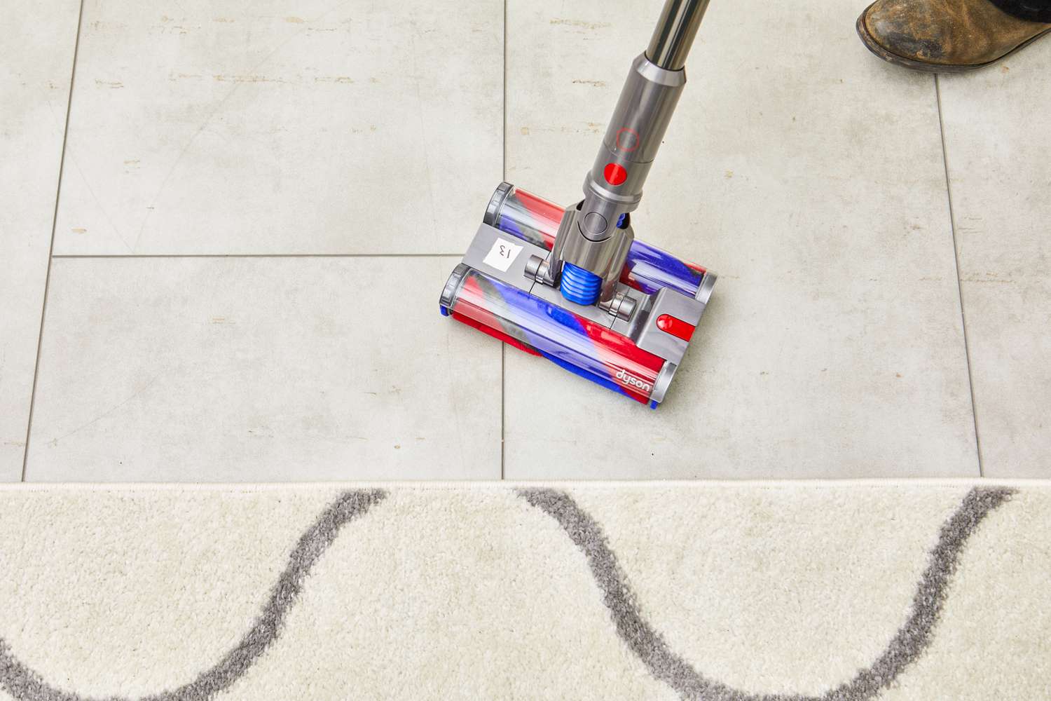 Dyson Omni-Glide+ Cordless Vacuum cleaning a tile floor by a rug