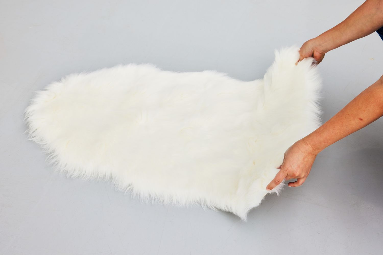 A person places the Ashler Faux Fur Rug on the ground