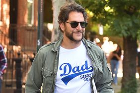 Bradley Cooper wears a "Dad Since 2017" tee shirt while out in New York City. The American actor showed off a new beard style and finished his look in a green jacket, grey trousers, and Nike Air Jordans. 06/11/2024