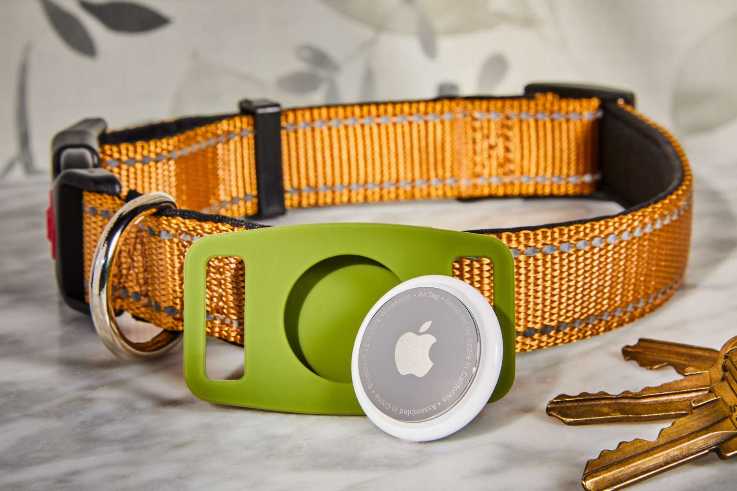 Apple AirTag with green holder, dog collar, and keys displayed on marble countertop