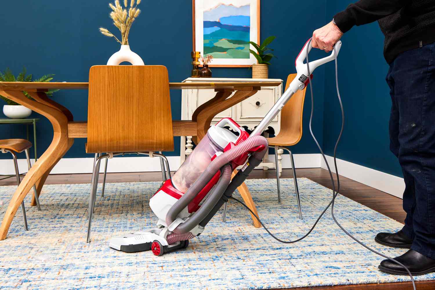 A person vacuums under a table and chairs using the Kenmore Allergen Seal Bagless Upright Vacuum